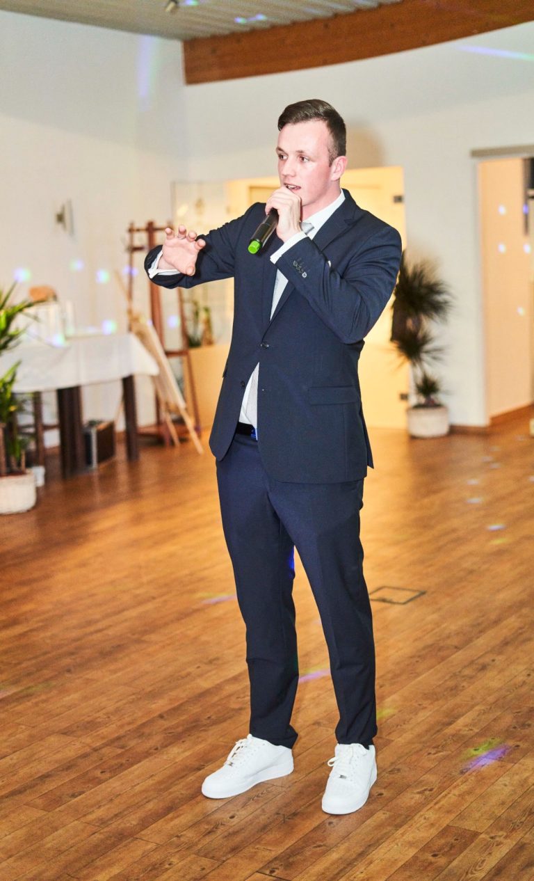 DJ Baumi hat hier ein Mikrofon in der Hand und stellt sich nett bei den Gästen vor.